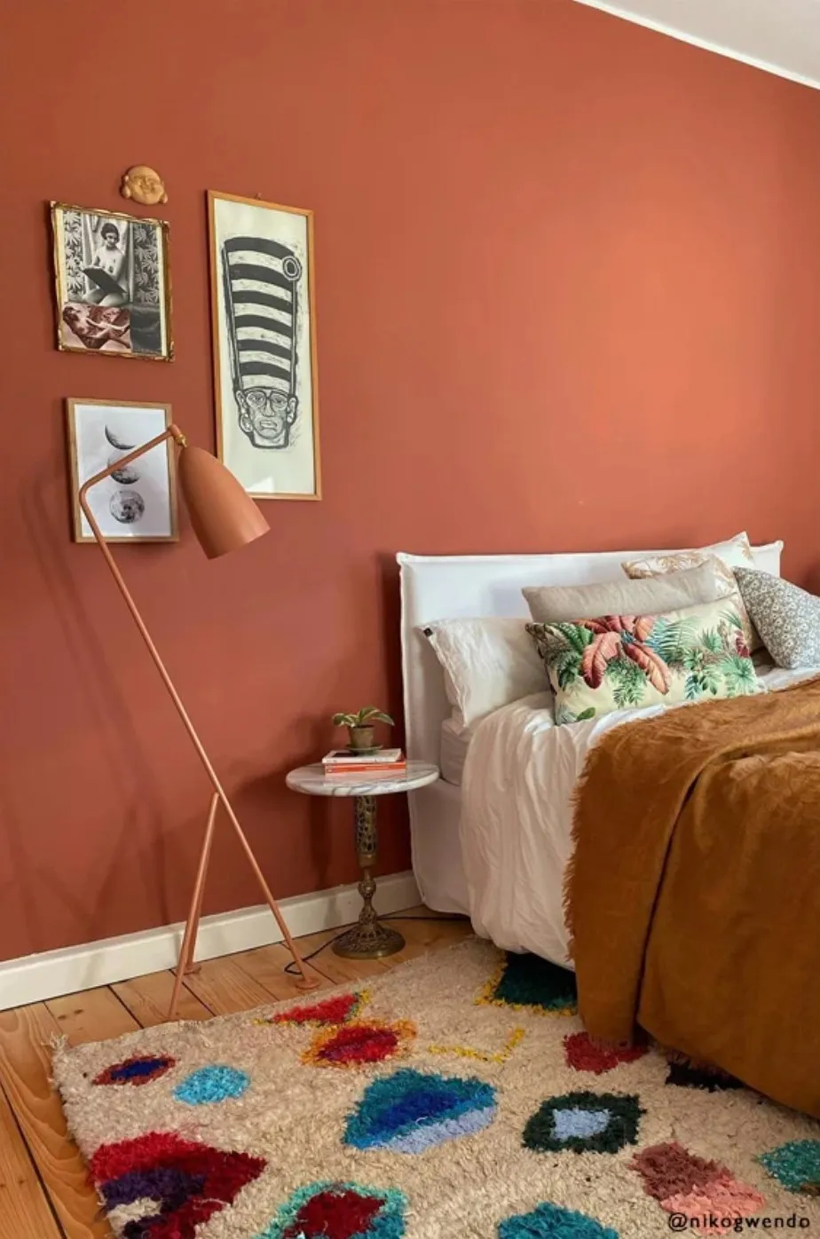Bedroom painted in a warm red terracotta colour with a colourful rug and neutral bedding