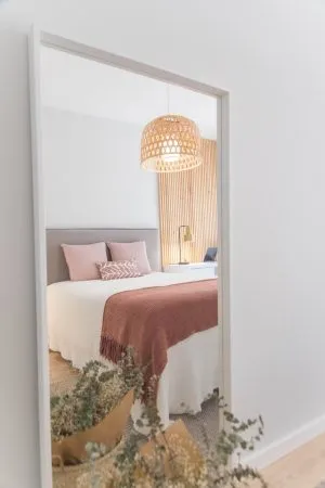 A white bedroom in a vacation home with a grey headboard and a pink throw on the bed