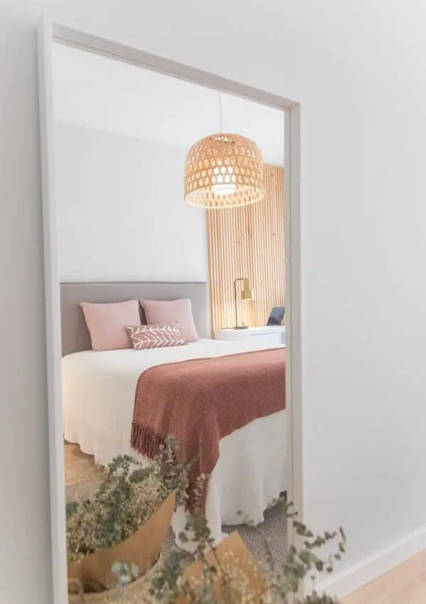 A white bedroom in a vacation home with a grey headboard and a pink throw on the bed
