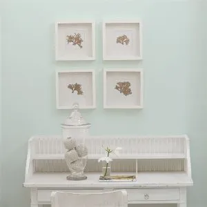 Living room wall painted in eau de nil with a white desk and four white framed prints on the wall