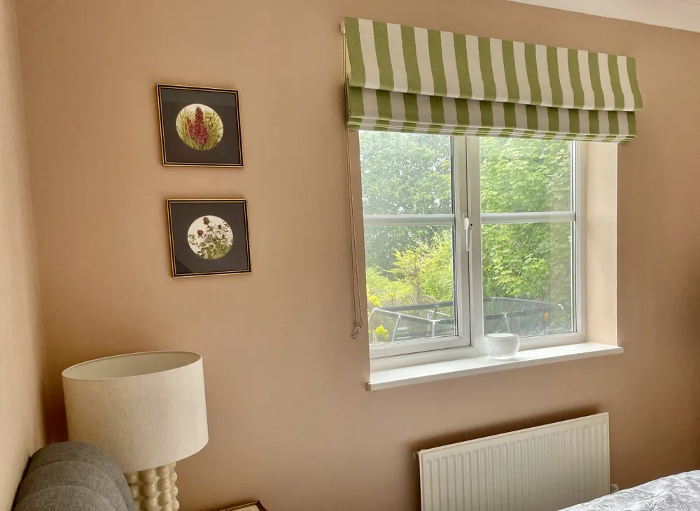 Green and white striped roman blinds against pink walls