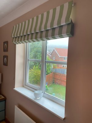 Green and white striped roman blinds against walls painted in Setting Plaster by Farrow and Ball