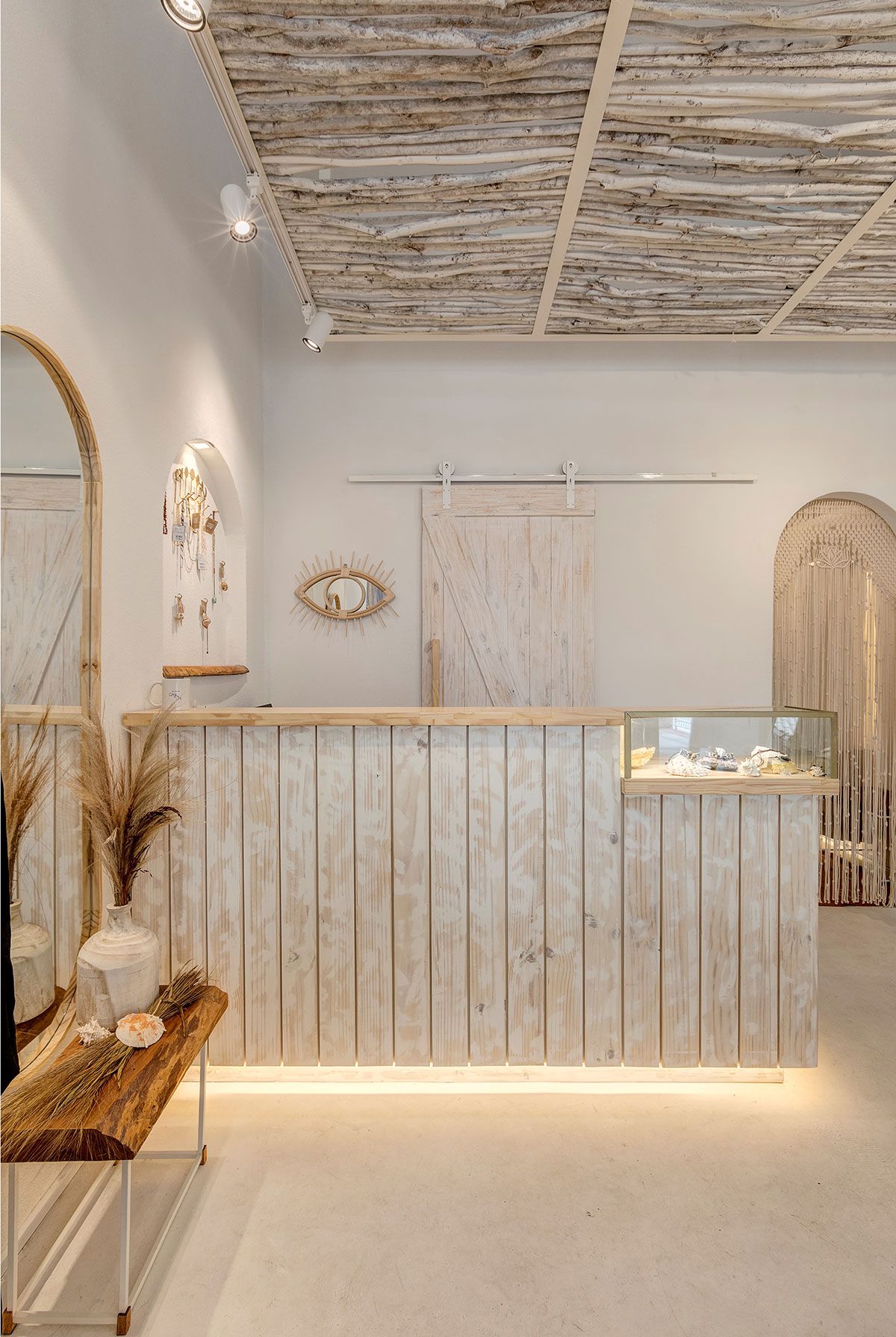 Boho inspired boutique shop design with a wooden shop counter featuring a glass display case on one side.