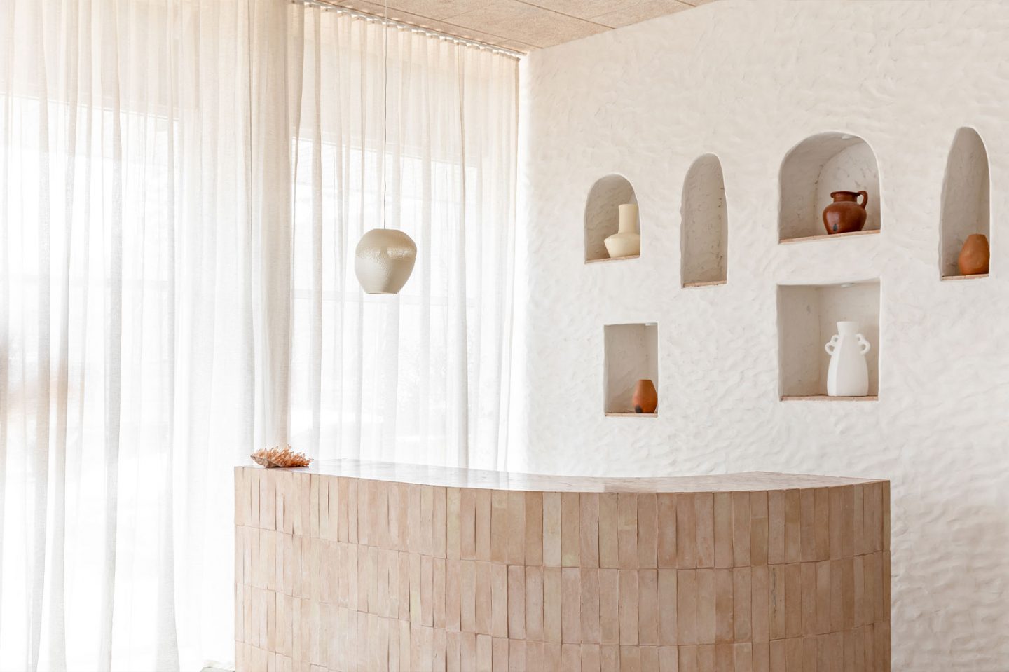 Calming and serene salon design with a curved counter covered in light pink-terracotta tiles. Mediterranean style.