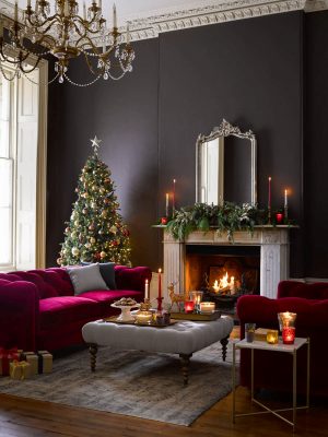 Cosy Christmas living room with a pink velvet sofa and black walls. Candles on the coffee tables and side tables, and the fire creating an atmospheric glow