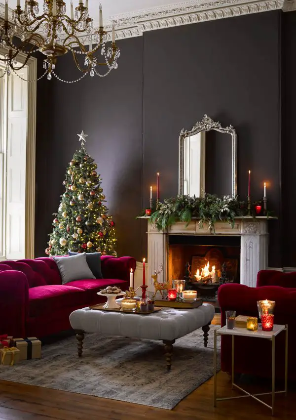 Cosy Christmas living room with a pink velvet sofa and black walls. Candles on the coffee tables and side tables, and the fire creating an atmospheric glow