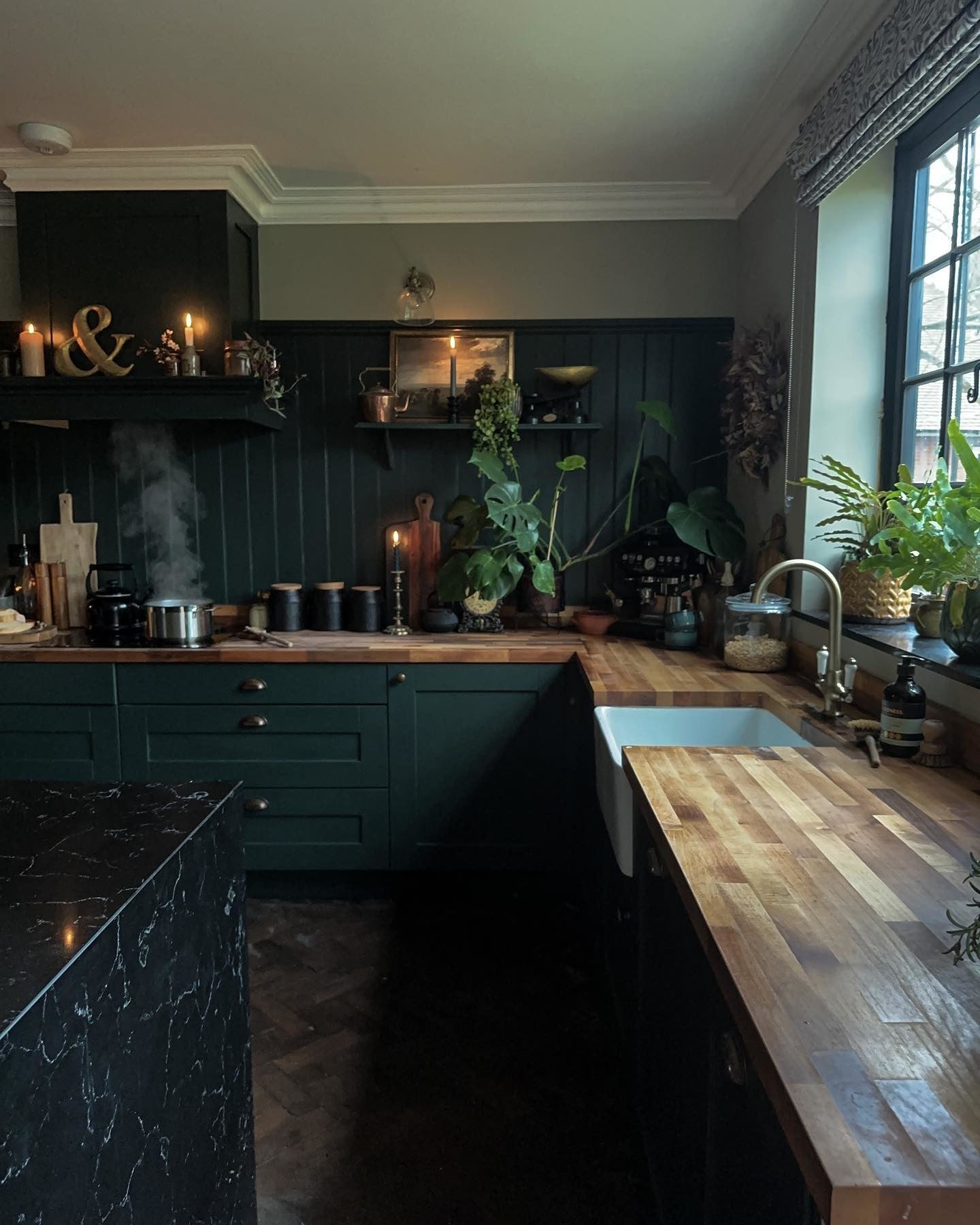 A dark academia aesthetic kitchen with wooden worktops and cabinetry painted in dark green