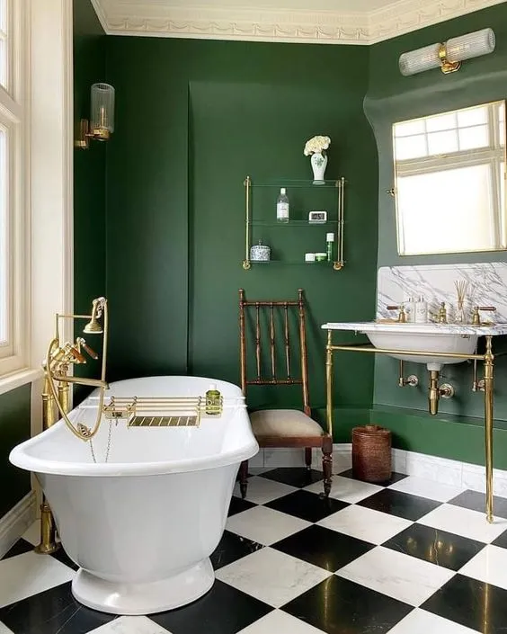 A traditional bathroom painted in duck green by Farrow and Ball with a black and white checked floor and a white freestanding rollmop bath.