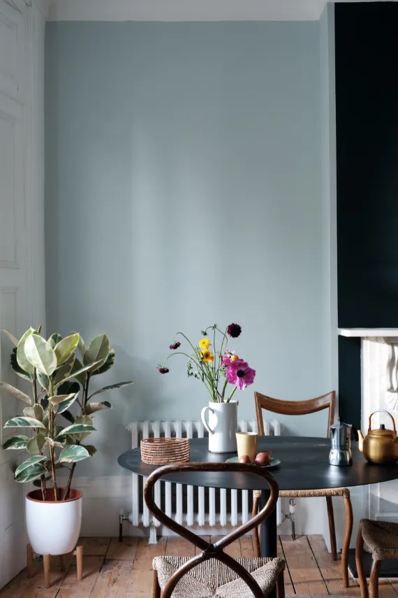 Dining room painted in Pastel blue. The paint colour is Borrowed Light by Farrow and Ball. A round table for two in a dark wood finish with a bunch of colourful flowers on the table.