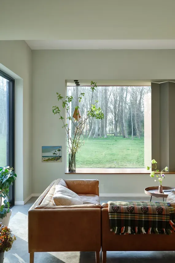 Living room painted in pastel green, the shade is Eddy by Farrow and ball. There is a large corner leather sofa.